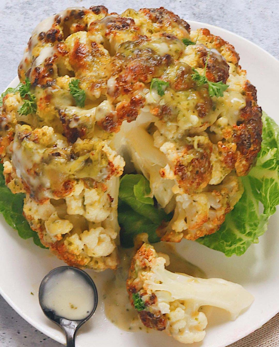 Whole Roasted Cauliflower with Cheesy Pesto served on a plate with spoon.