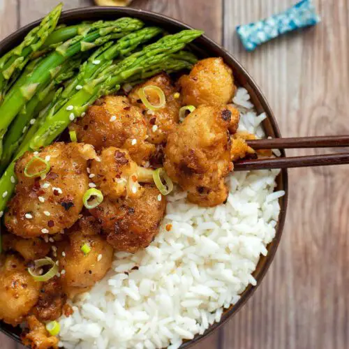 Orange Cauliflower with Steamed Asparagus recipe served in a bowl with chopsticks.