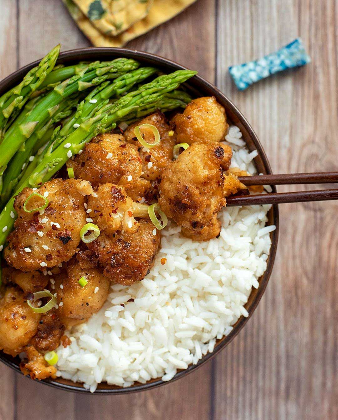 Orange Cauliflower with Steamed Asparagus recipe served in a bowl with chopsticks.